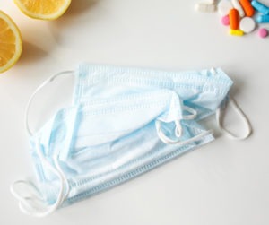 Maseczka chirurgiczna leży na stole, obok połówkii cytryny i kolorowe pigułki.