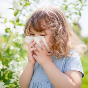 Dziewczynka wydmuchuje nos na tle kwitnących roślin